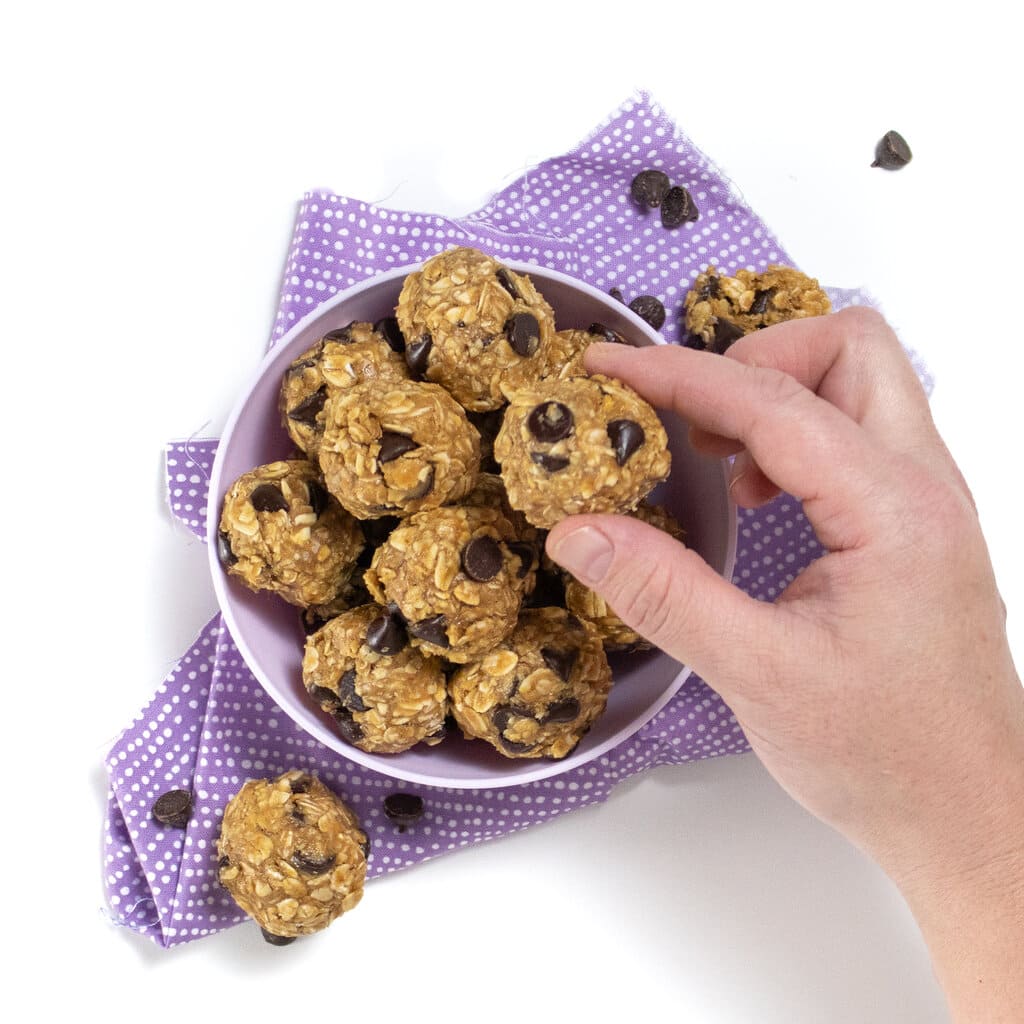 A purple ball full of lactation energy balls with a hand reaching to grab one.