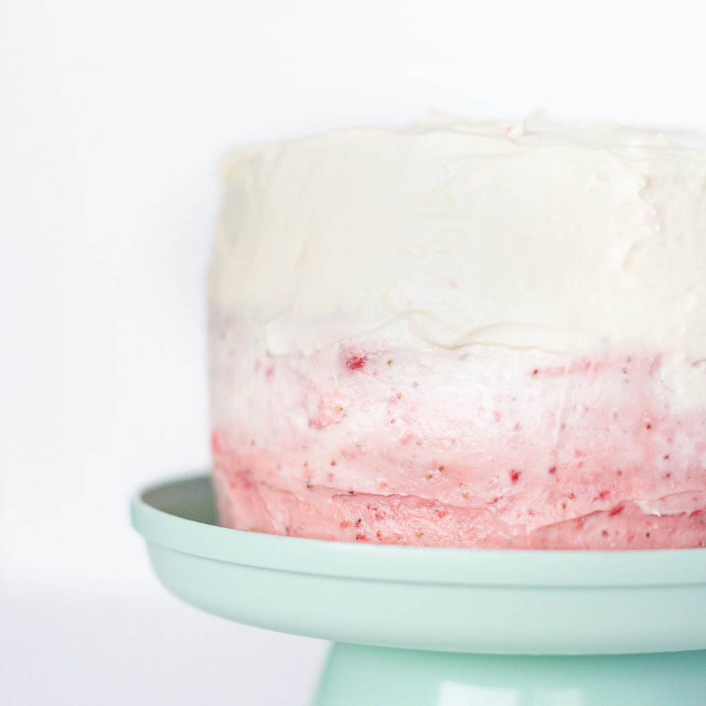 Up close of a ombre smash cake with white and pink frosting on a teal cake stand against a white background.