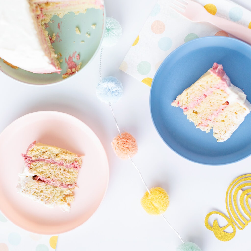 Spread of a smash cake and she was like for the cake on a pink and blue kids plate with birthday decorations in pastel colors spread around a white background.