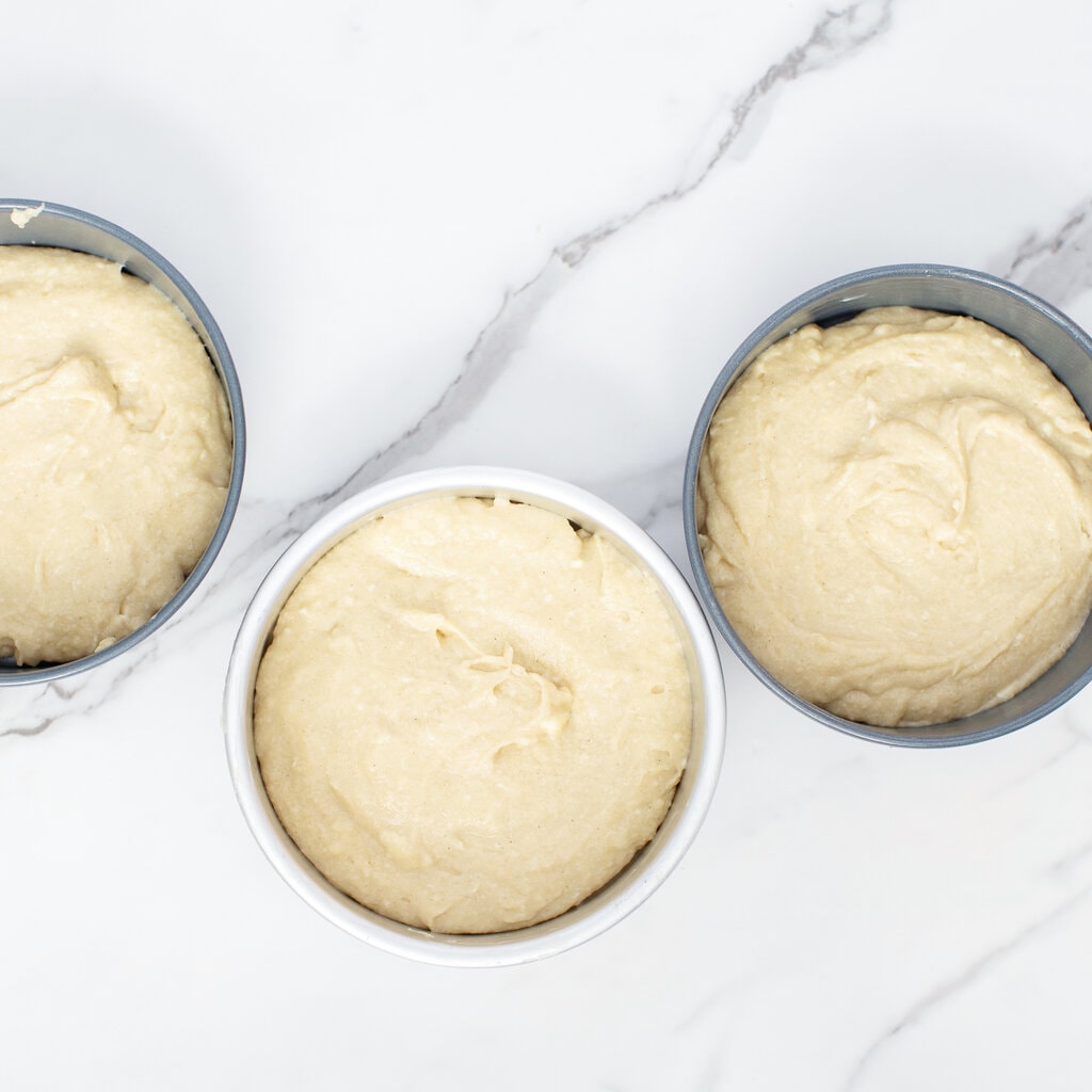 Three round cake pans with batter in them.