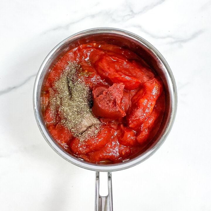 Silver saucepan on a marble surface with ingredients inside for a pizza sauce for kids.