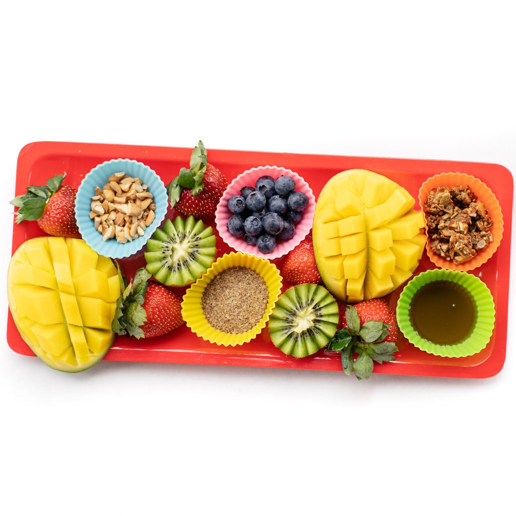 Orange tray full of colorful fruits and toppings for a yogurt parfait's.