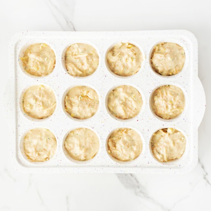 A muffin tray full of veggie muffins ready to be baked on a marble countertop.