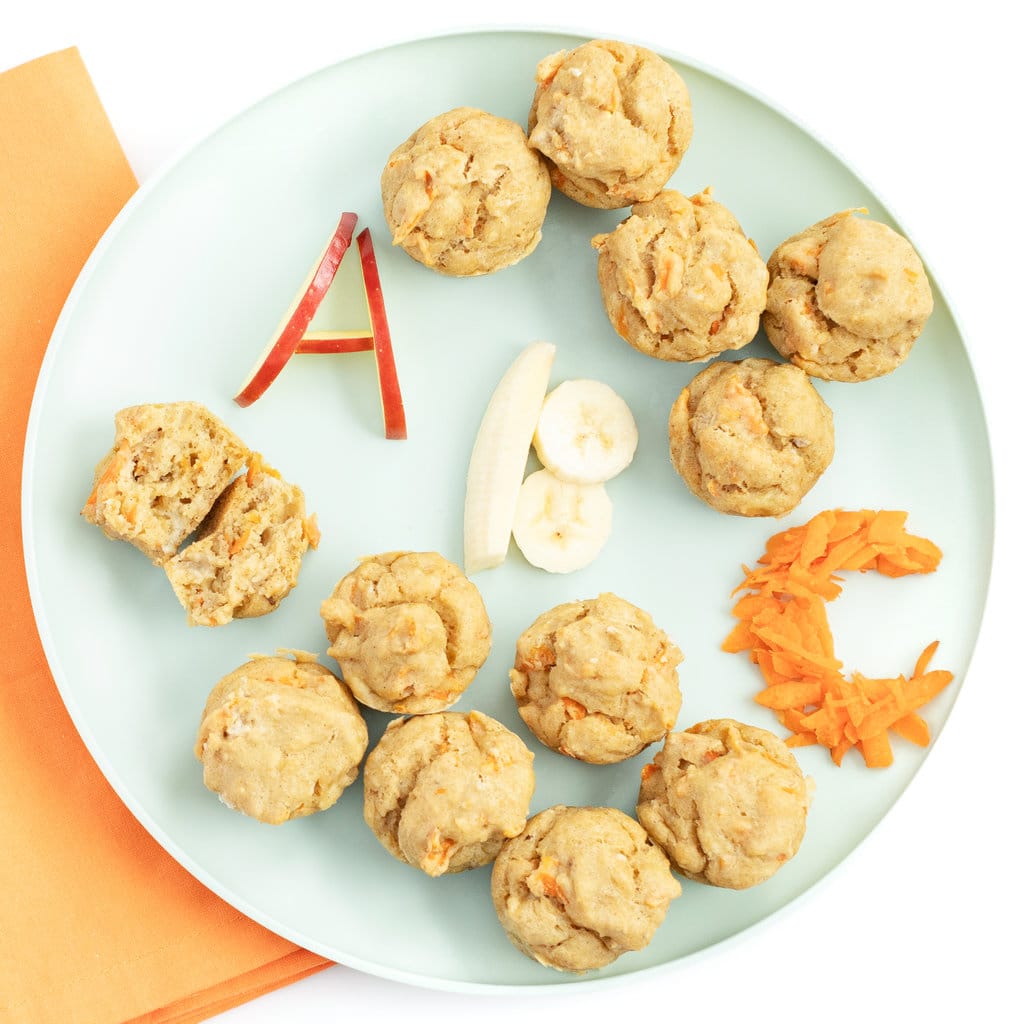 Teal kids play with ABC muffins with the letters a, B, C written out in Apple, banana and carrots again say marble background with a orange napkin all on my white kitchen counter. 