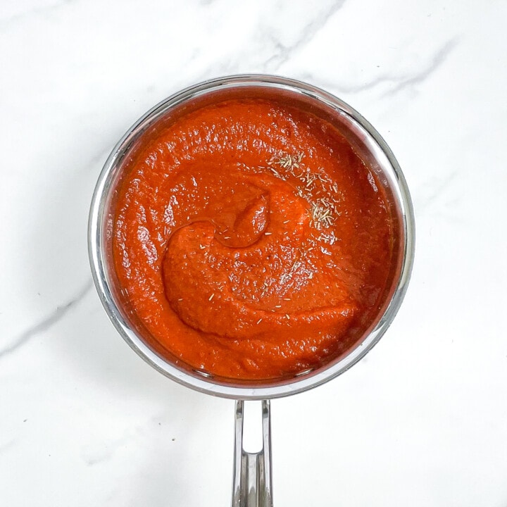 Silver saucepan on a marble surface with cooked pizza sauce blended.