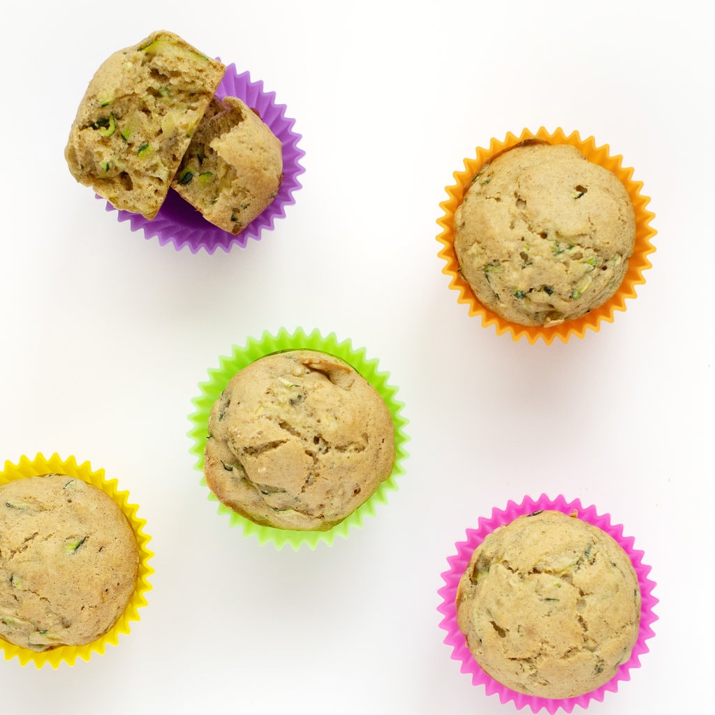 zucchini muffins in colorful cupcake silicone liners on a white surface.