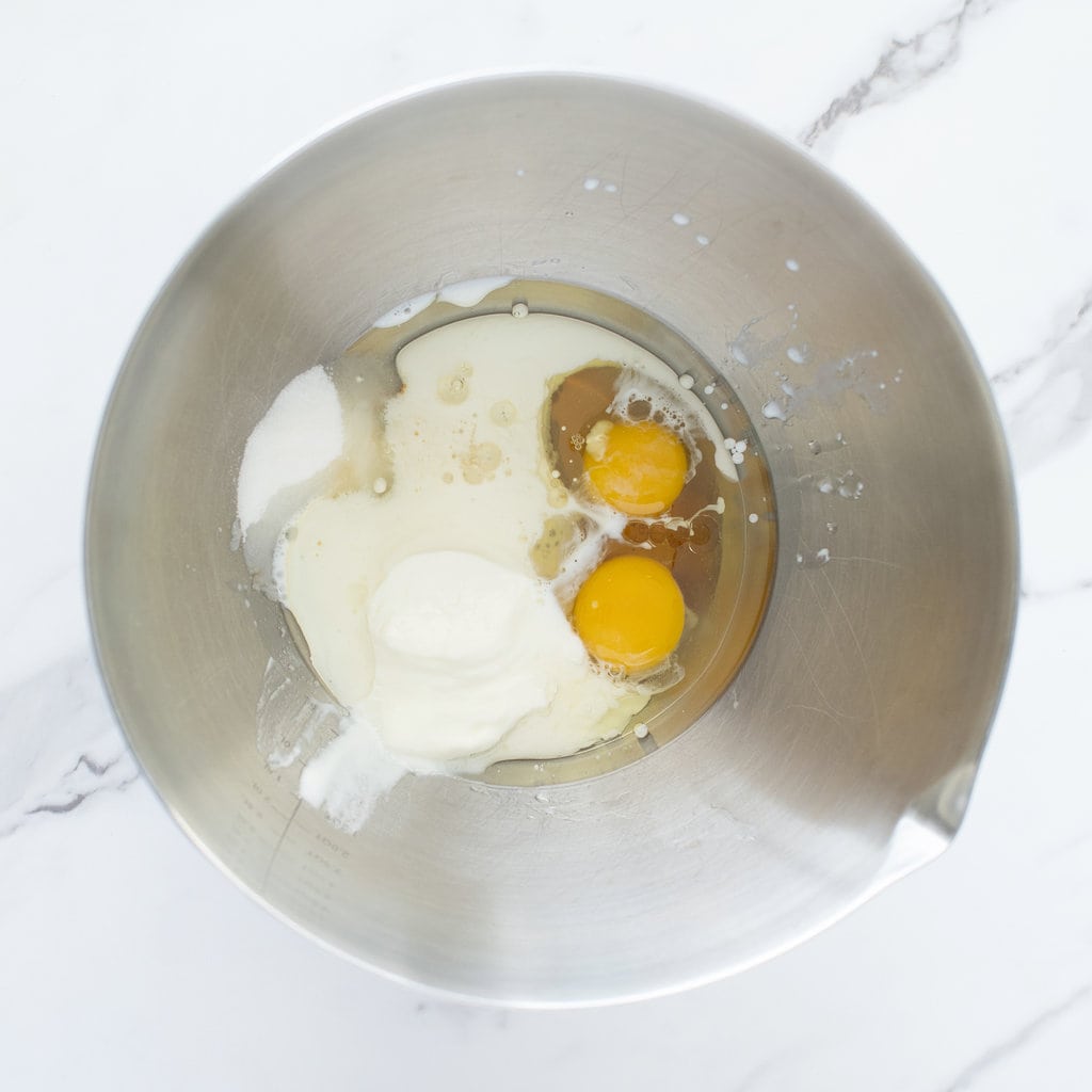 Hey silver mixing bowl with wet ingredients for muffins against a way to marble counter.