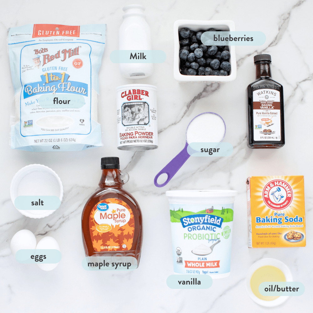 Spread of ingredients for blueberry muffins on a marble countertop with graphics telling what the items are.