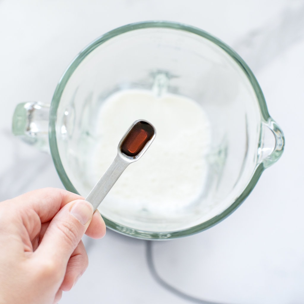 A hand pouring in Maple syrup syrup blender full of milk on a white marble countertop.