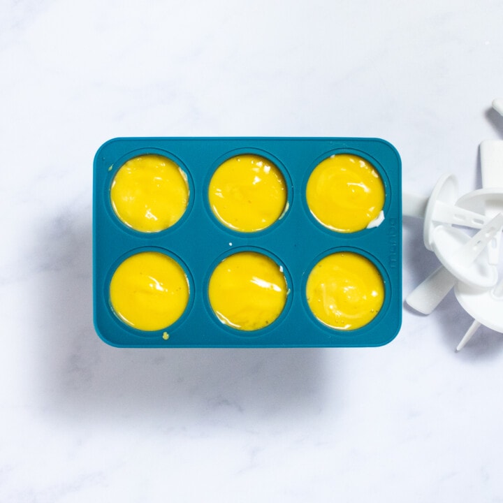 A dark teal popsicle mold filled with mango purée about to be frozen.