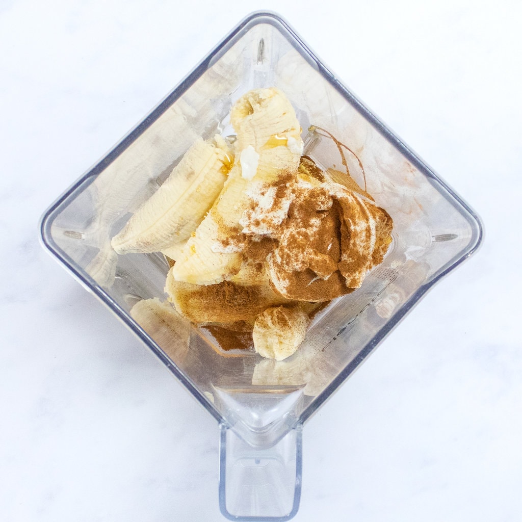 Clear blender with bananas, cinnamon, yogurt and honey ready to get pureed.