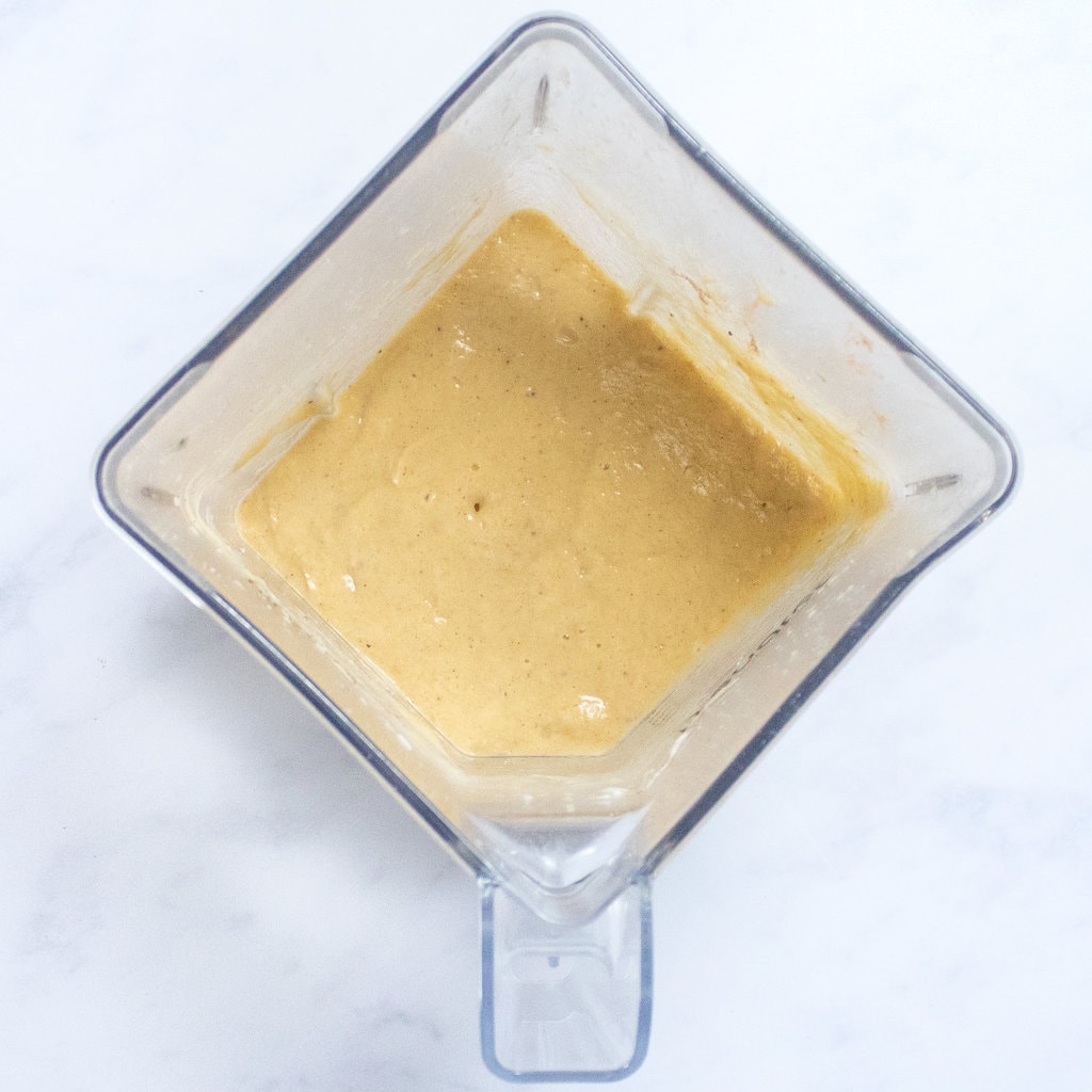 Pureed ingredients for banana popsicles in a blender on a white marble counter.