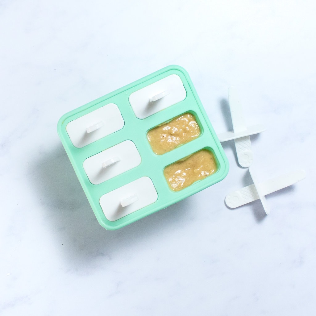 A teal popsicle mold full of banana popiscles ready to get placed in the freezer.