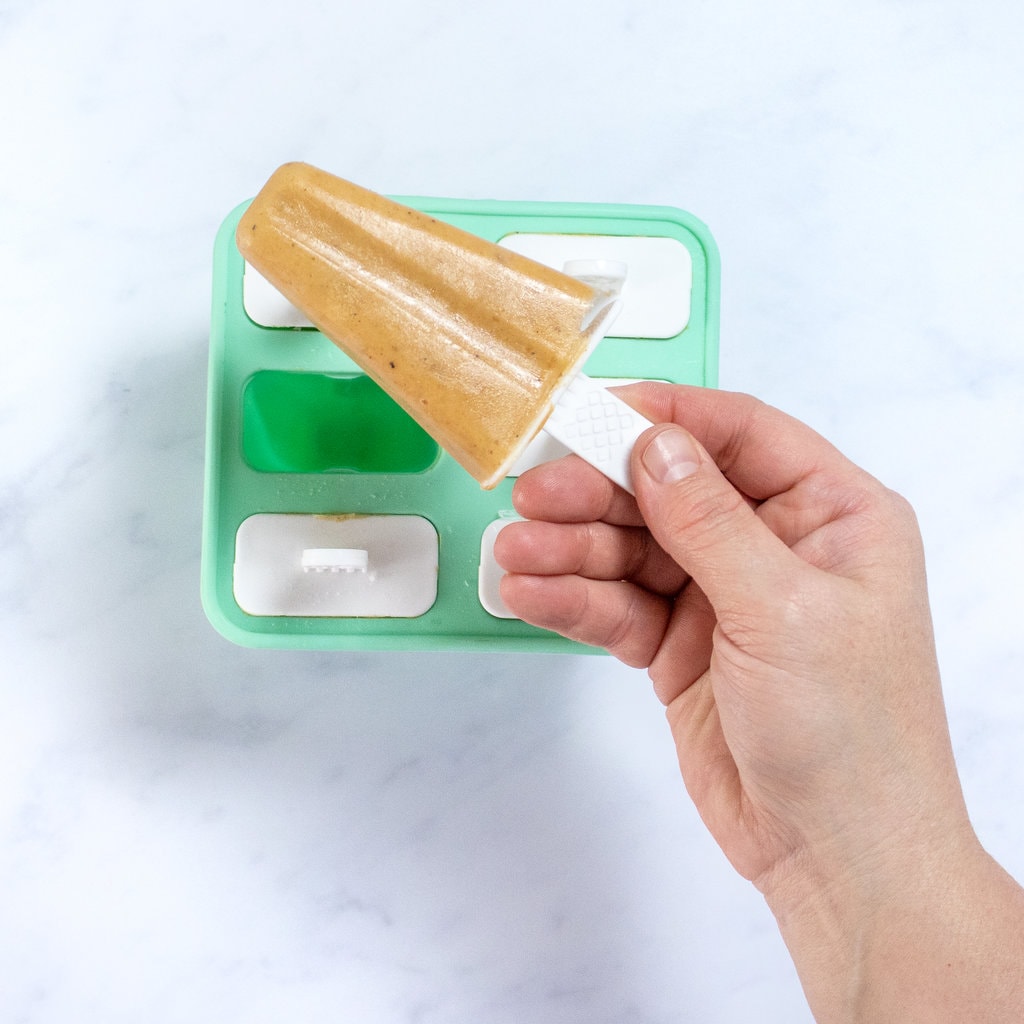 A hand holding a banana popsicle over the popsicle tray.
