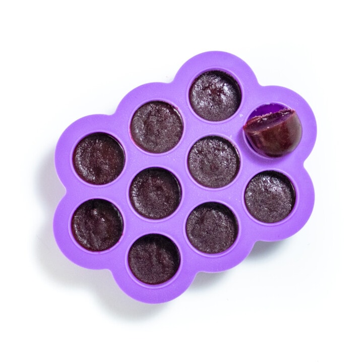 Purple freezer tray full of frozen blackberry baby food purée against a white background