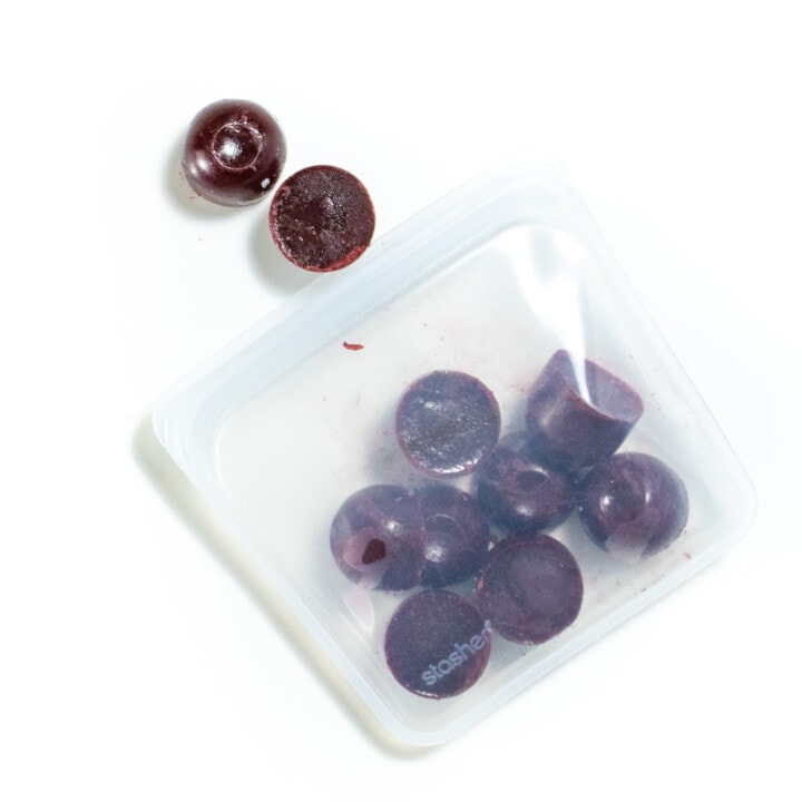 A clear stasher bag full of frozen round cubes of blackberry puree.