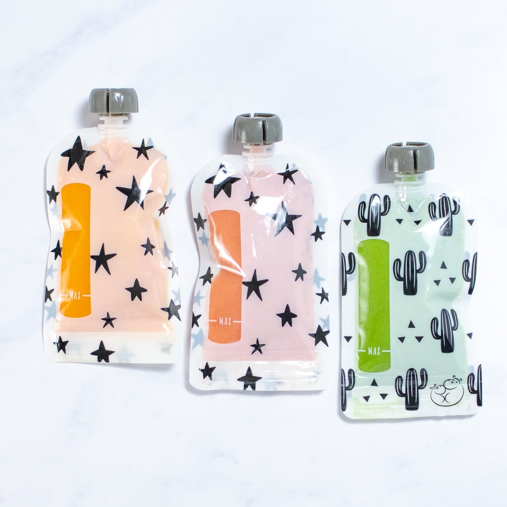Three baby food pouches with homemade purées lined up on a marble countertop.