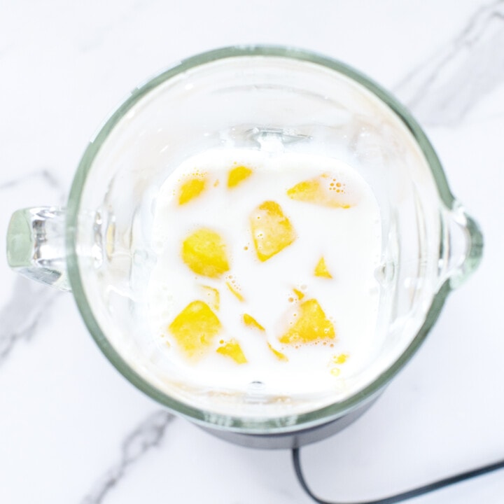 Clear glass blender with milk, mango, maple syrup and vanilla extract getting ready to blend into milk.