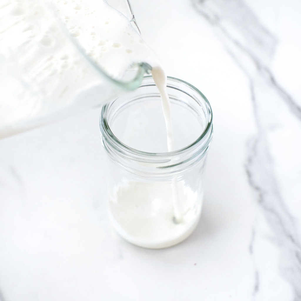 A clear glass blender point in vanilla milk to a clear glass on a white marble countertop.