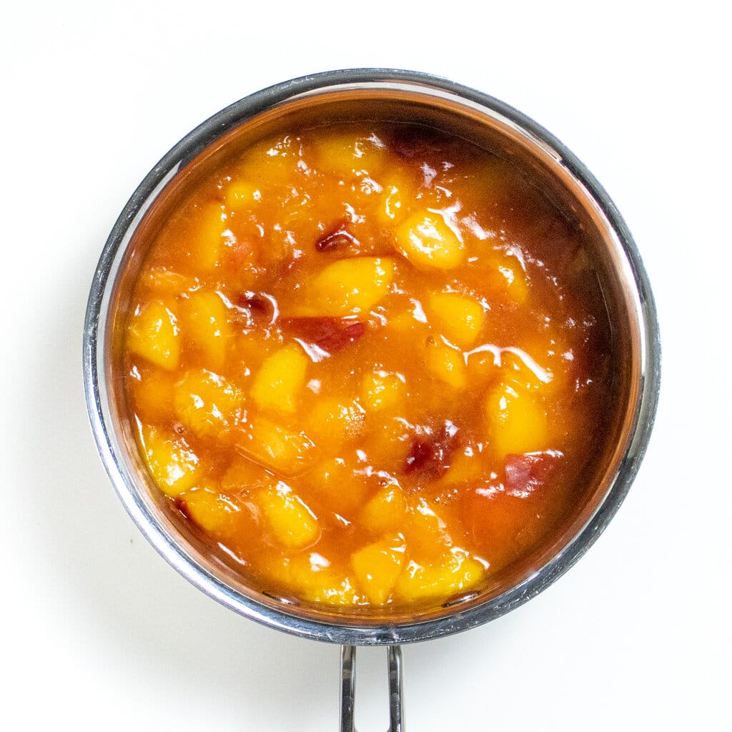 Simmered nectarines that are tender and flavored with cinnamon on a white background.