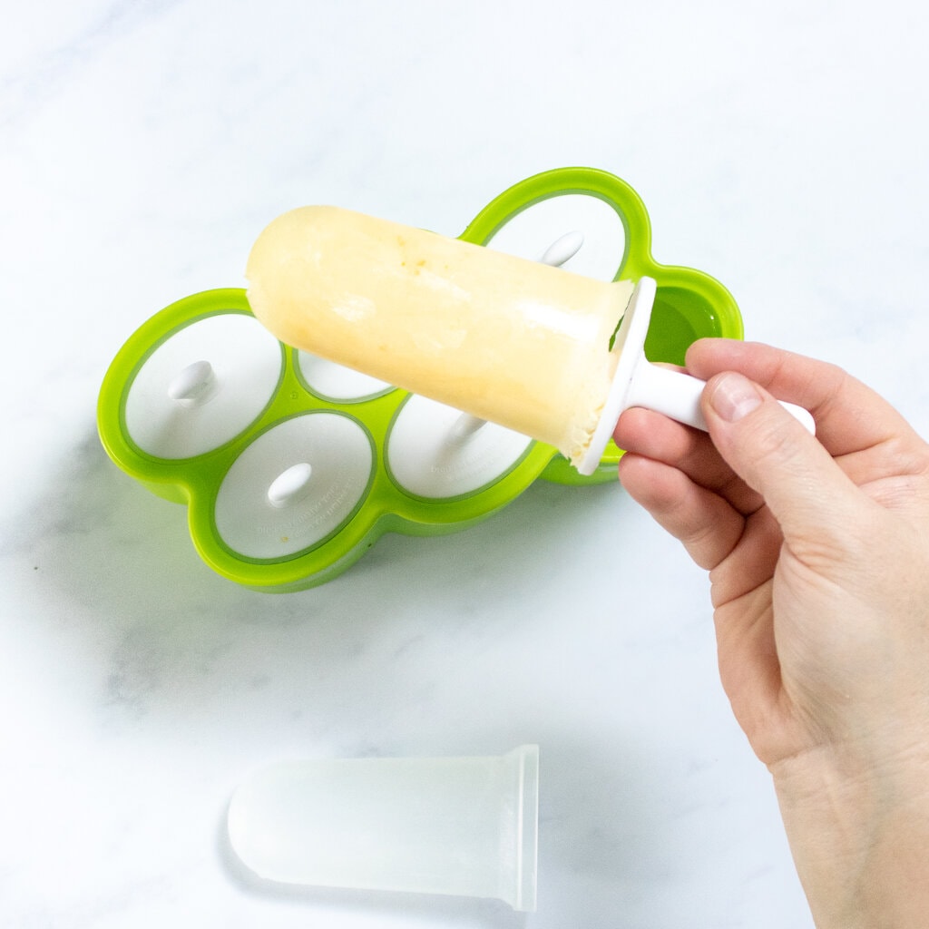 Hey Hannah holding a frozen orange Creamsicle over a popsicle mold.
