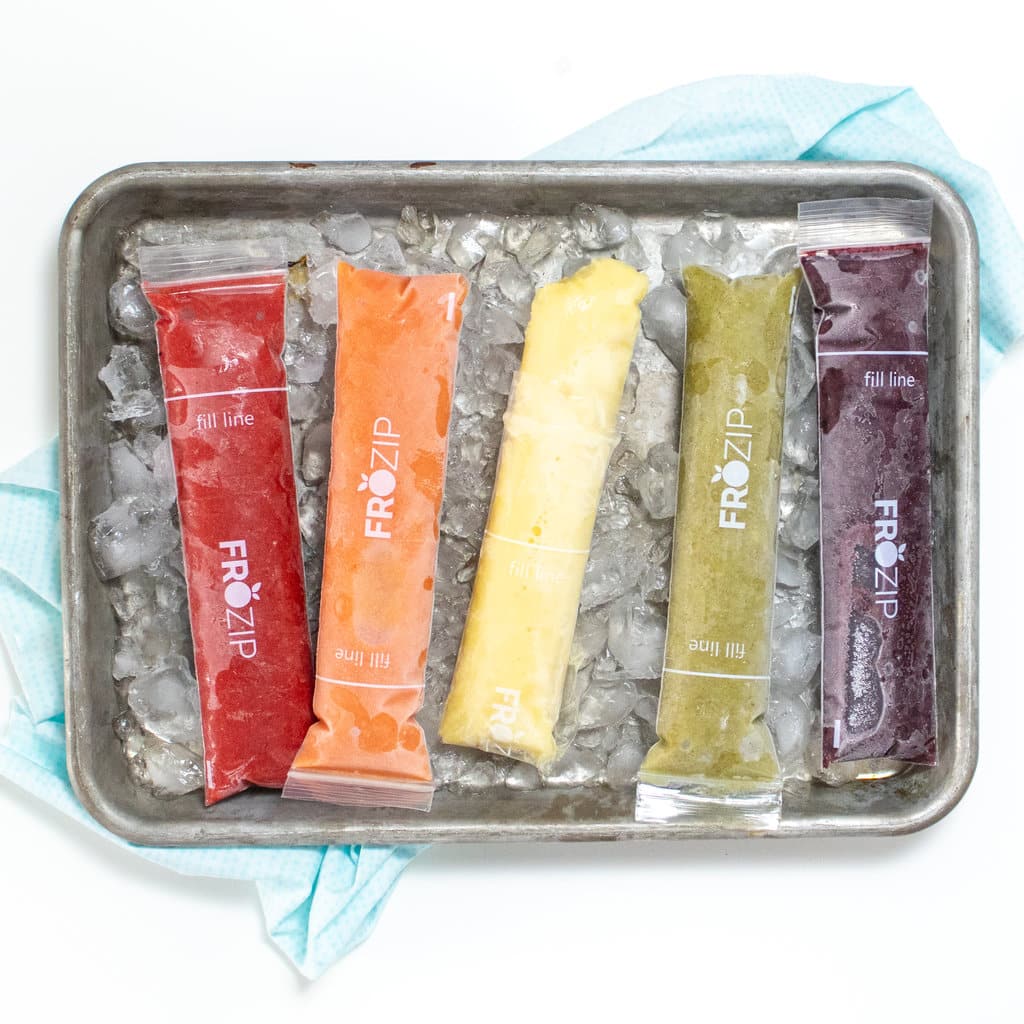 Small silver baking sheet with freezer pops in a rainbow color with ice and a blue napkin.