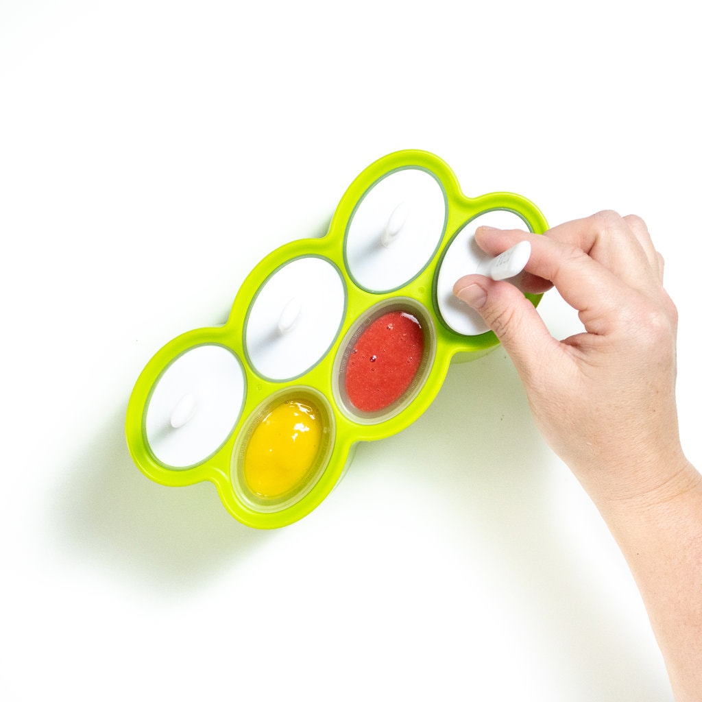 Hand placing the a popsicle stick into a popsicle mold full of fruit popsicles.