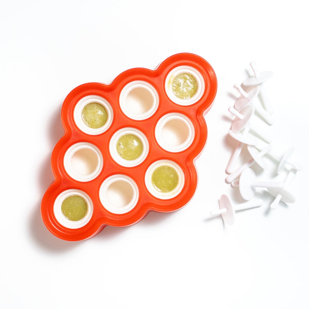 A red and white popsicle tray build with green grape popsicle liquid on a white background.
