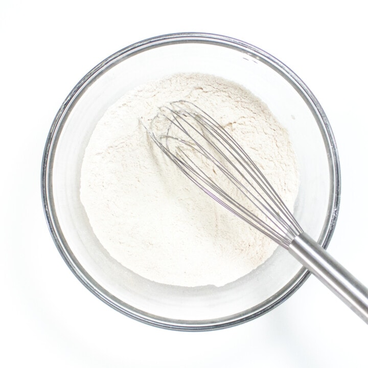 Clear glass mixing bowl with dry ingredients sitting on a white countertop.