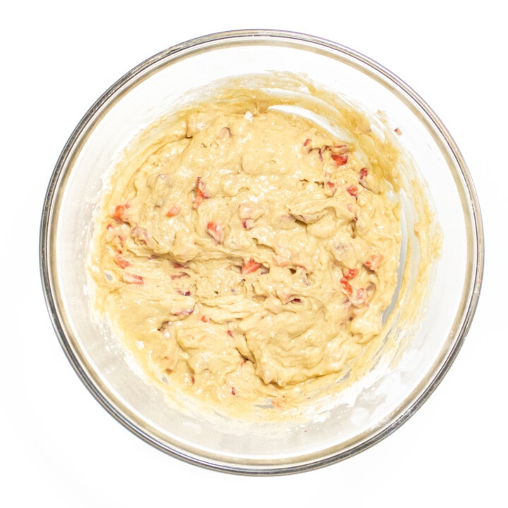 A clear bowl sitting on a white toner with strawberry muffin batter.