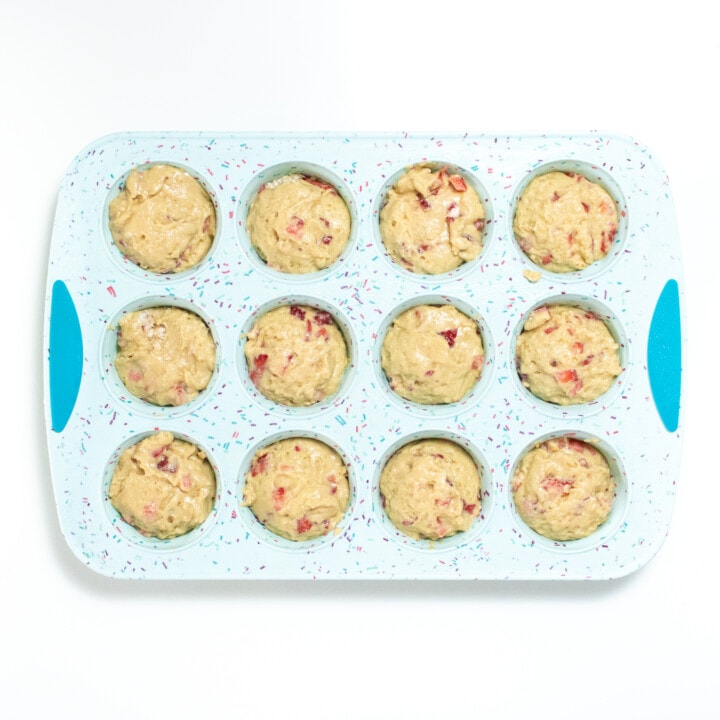 A blue muffin tin full with strawberry muffin batter against a white background.