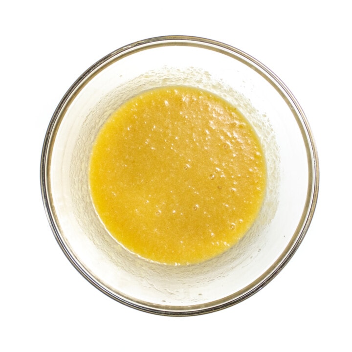 Clear glass baking bowl with wet ingredients inside sitting on a white counter.