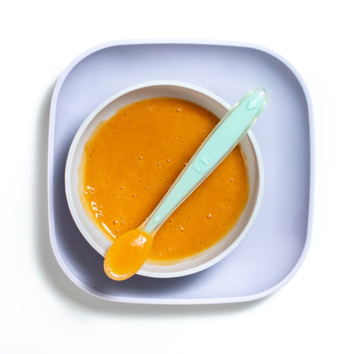 Purple baby plate and gray baby bowl filled with nectarine purée.