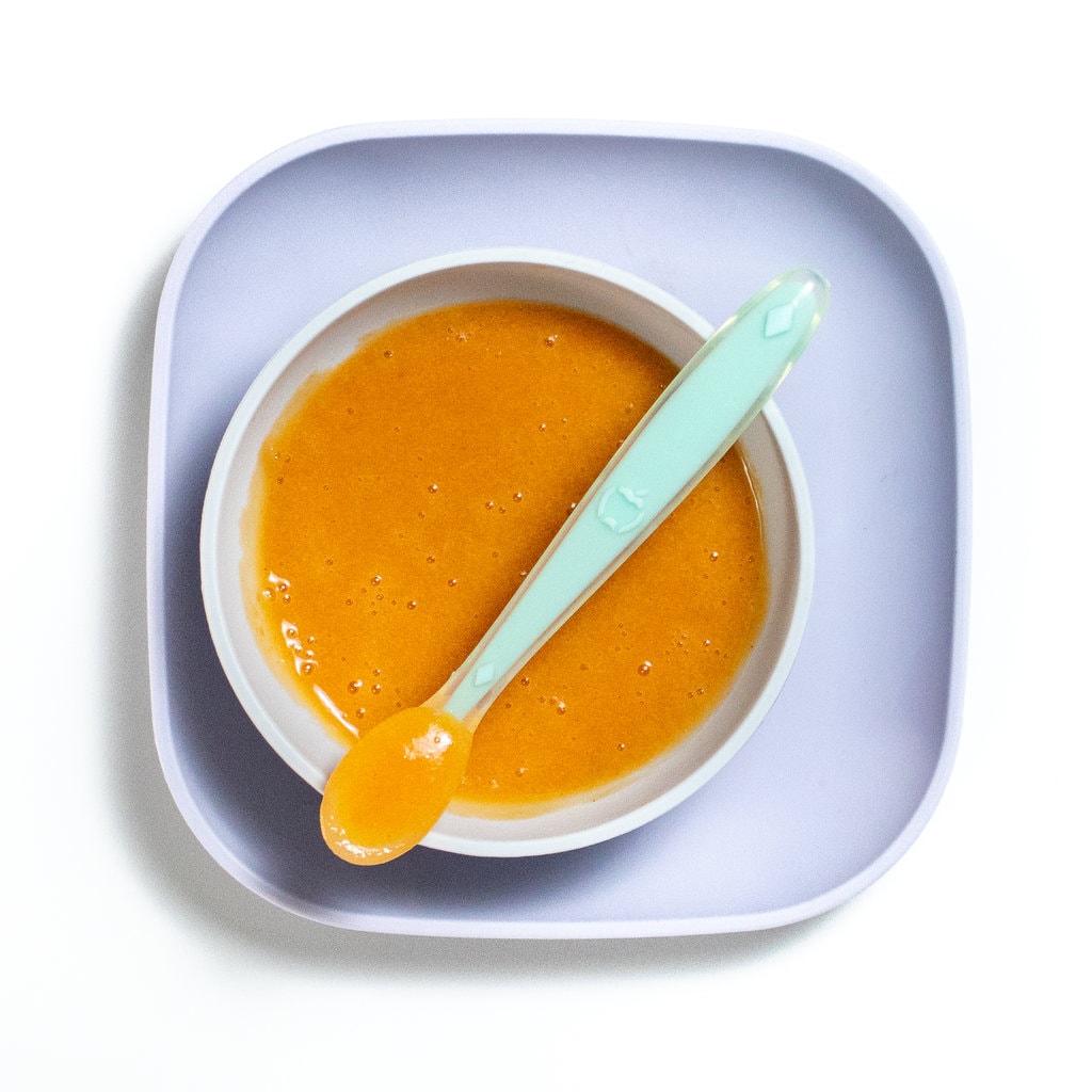 Purple baby plate and gray baby bowl filled with nectarine purée.