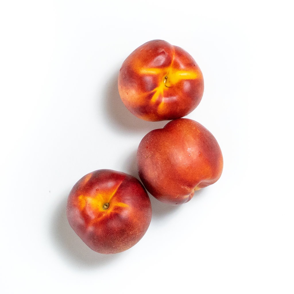 Three nectarine sitting on a weight counter.