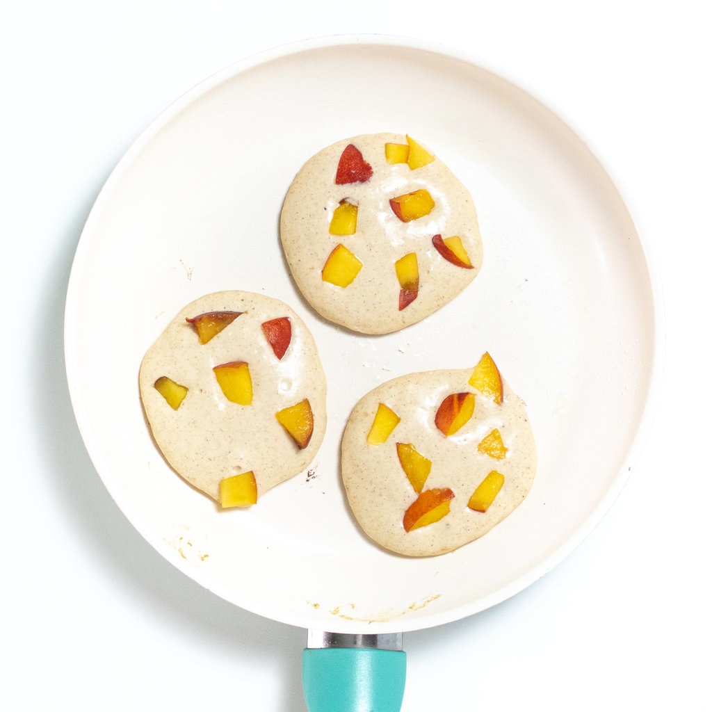 Three small pancakes with peaches on a cream skillet.