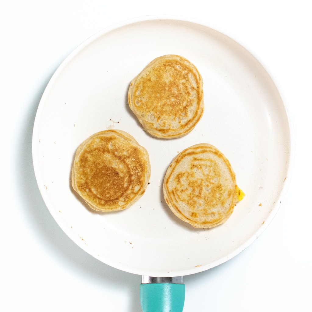 Three cooked peach pancakes on a cream skillet.