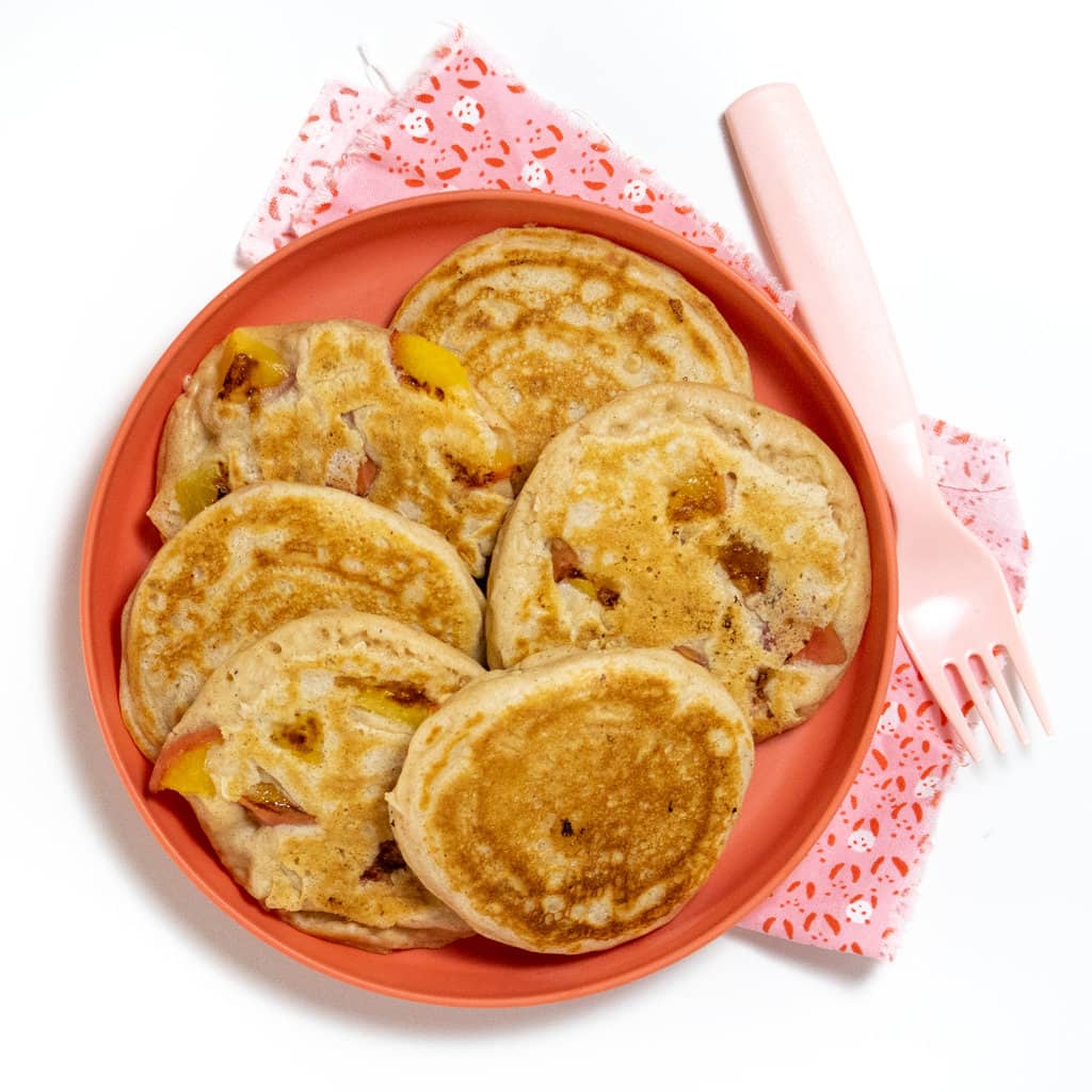 A pink kids play with a group of peach pancakes with a pink for compete against a white background.