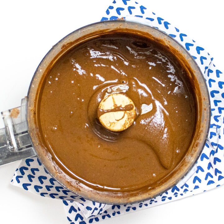 Food processor, full of very smooth, sun, butter. Against a white countertop with a blue and white napkin.