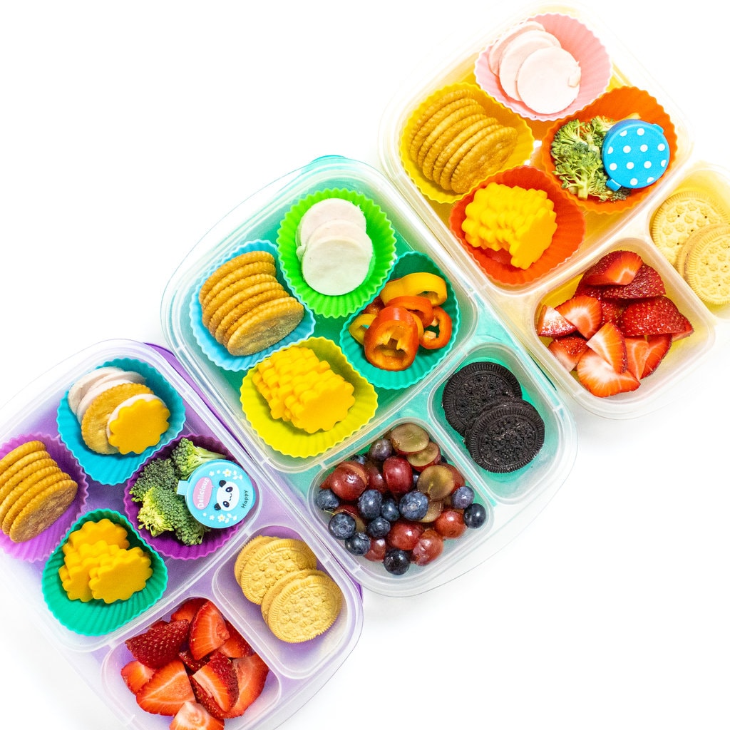 3 colorful kids lunch boxes full of ingredients to make lunchables plus different sides.