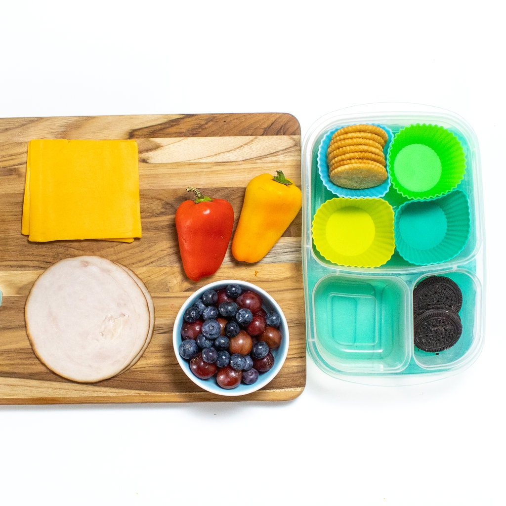A white counter with a cutting board and a lunch container for turkey lunchables.