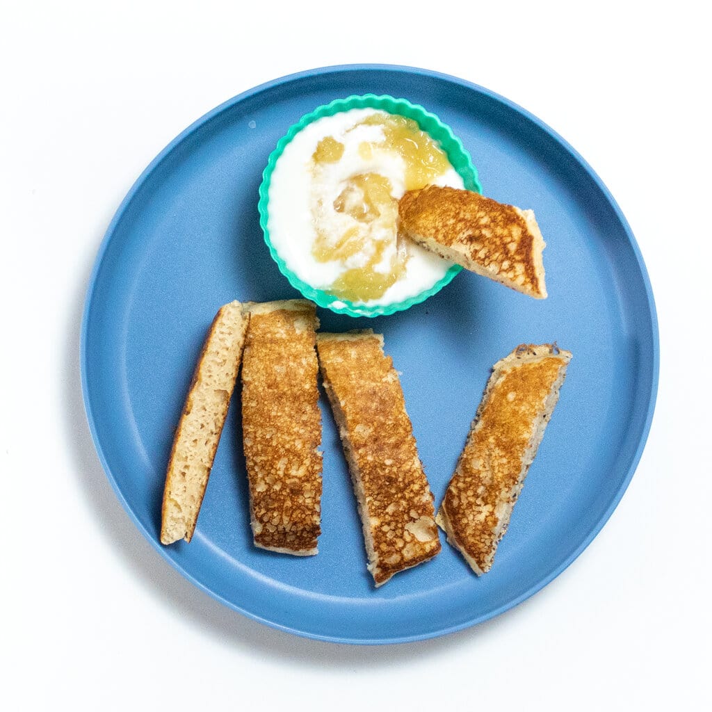 Blue kids plate with a applesauce pancake cut into strips for a dipping yogurt sauce.
