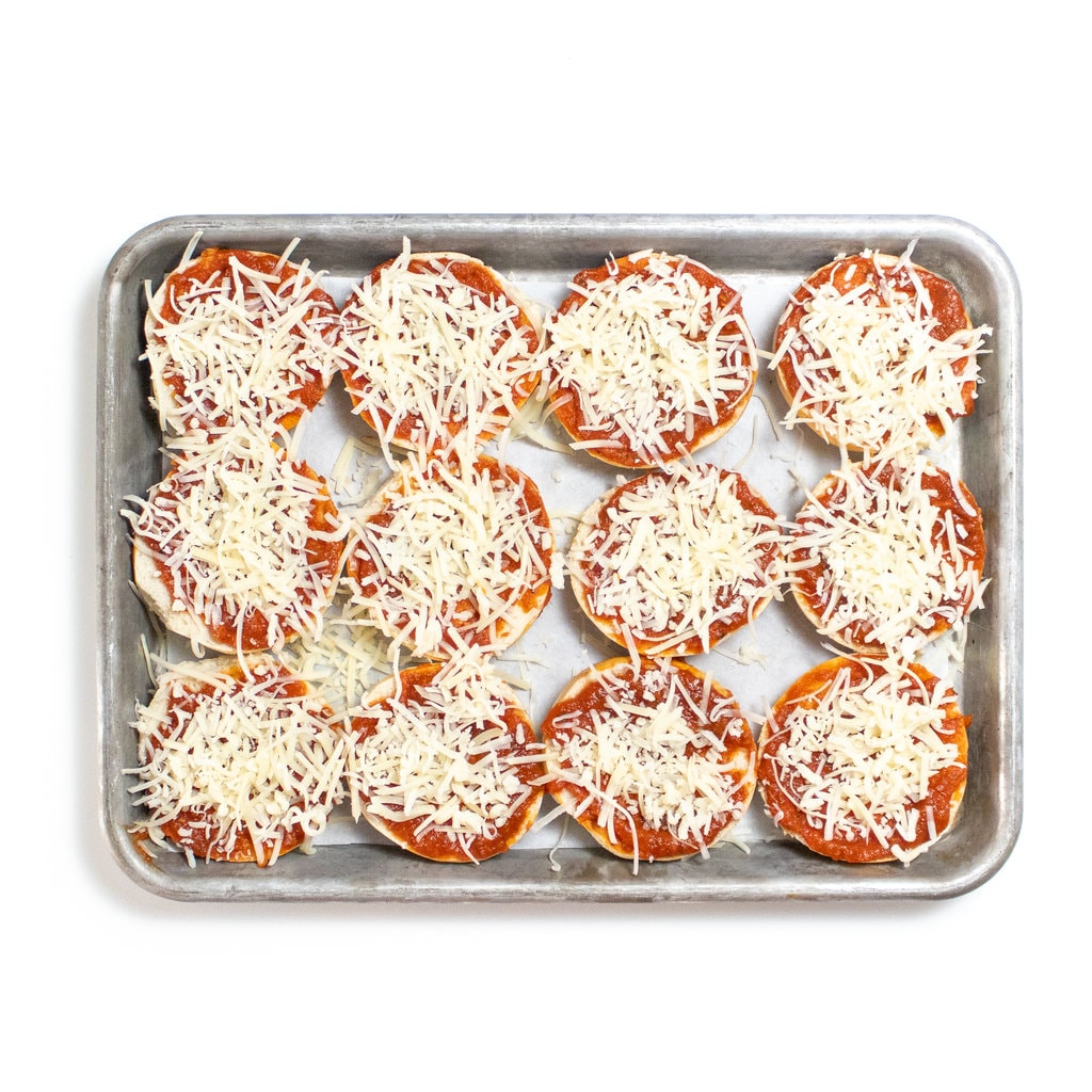 Mini bagel with cheese on a baking sheet on a white counter.