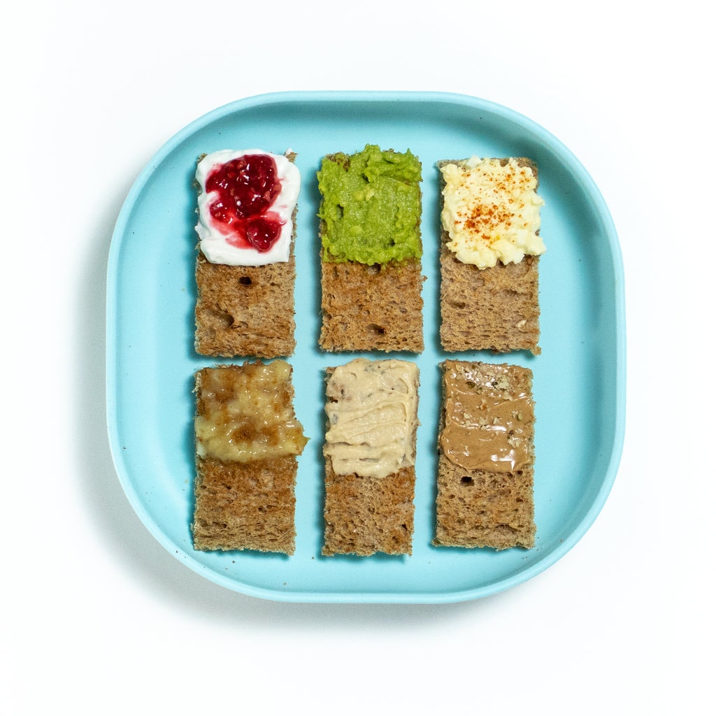 Teal baby plate with 6 different toasted bread and toppings.