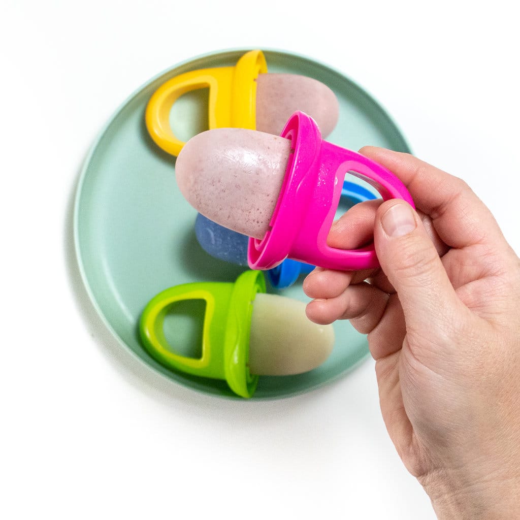 Hand holding a pink breastmilk popsicle over a plate of different flavors of popsicles.
