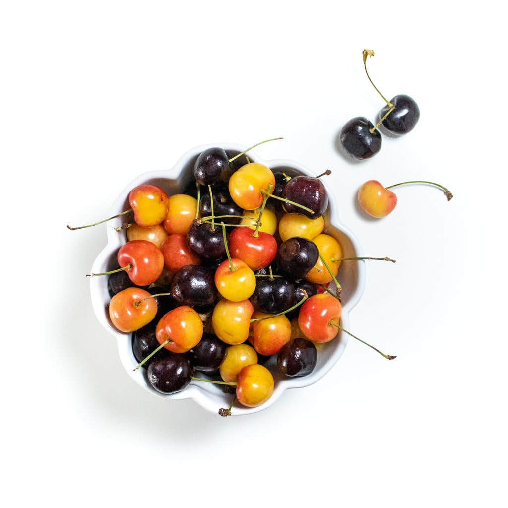 White scalloped bowl on a white counter with two different colors of cherries inside.