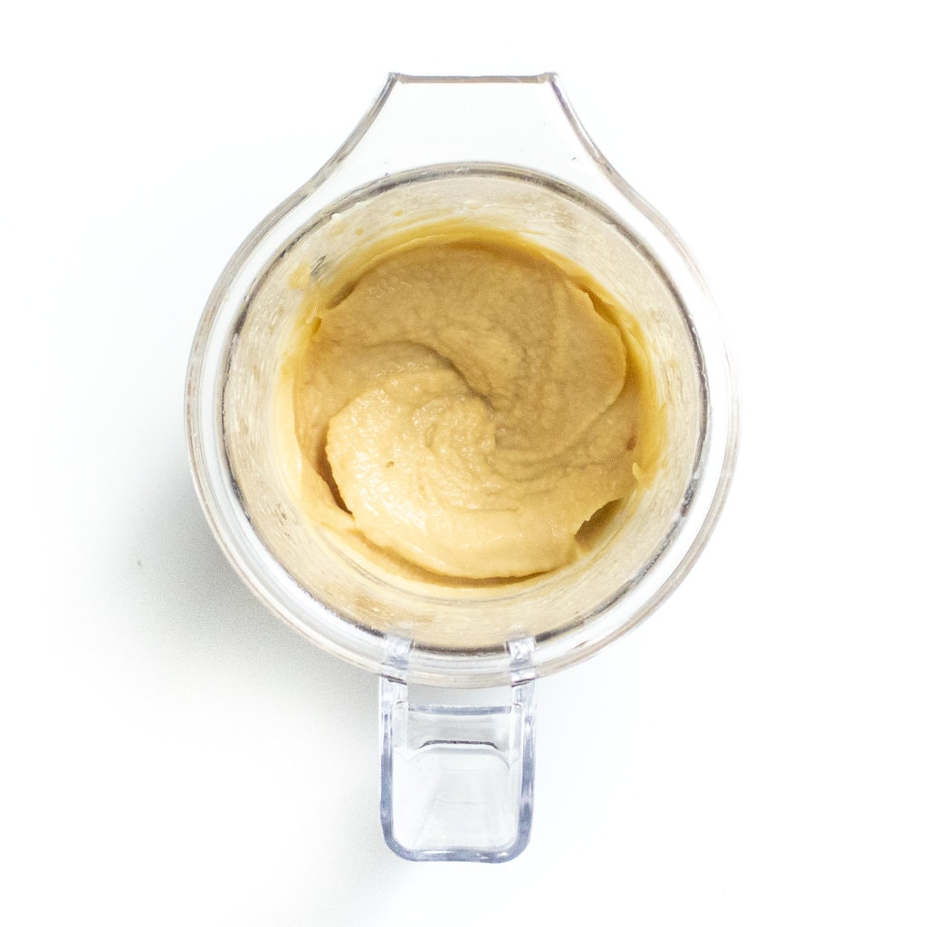 Clear blender on a white countertop full of chickpea puree.