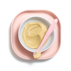Pink baby plate and bowl with chickpea puree inside.