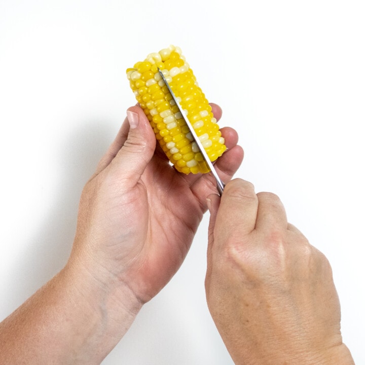 Hands cutting a corn cob row of kernels in half.