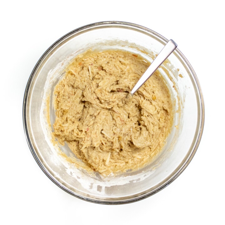 Clear white bowl on a white counter with apple muffin batter.